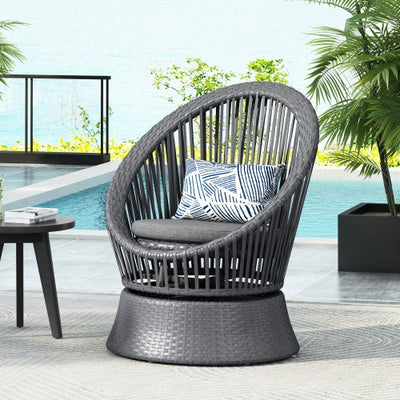 Gray wicker chair with a pillow on a patio with a pool and garden view.