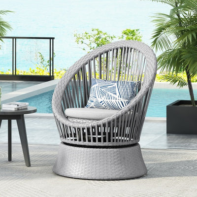 Gray wicker chair with a cushion on a patio with a pool and garden view.
