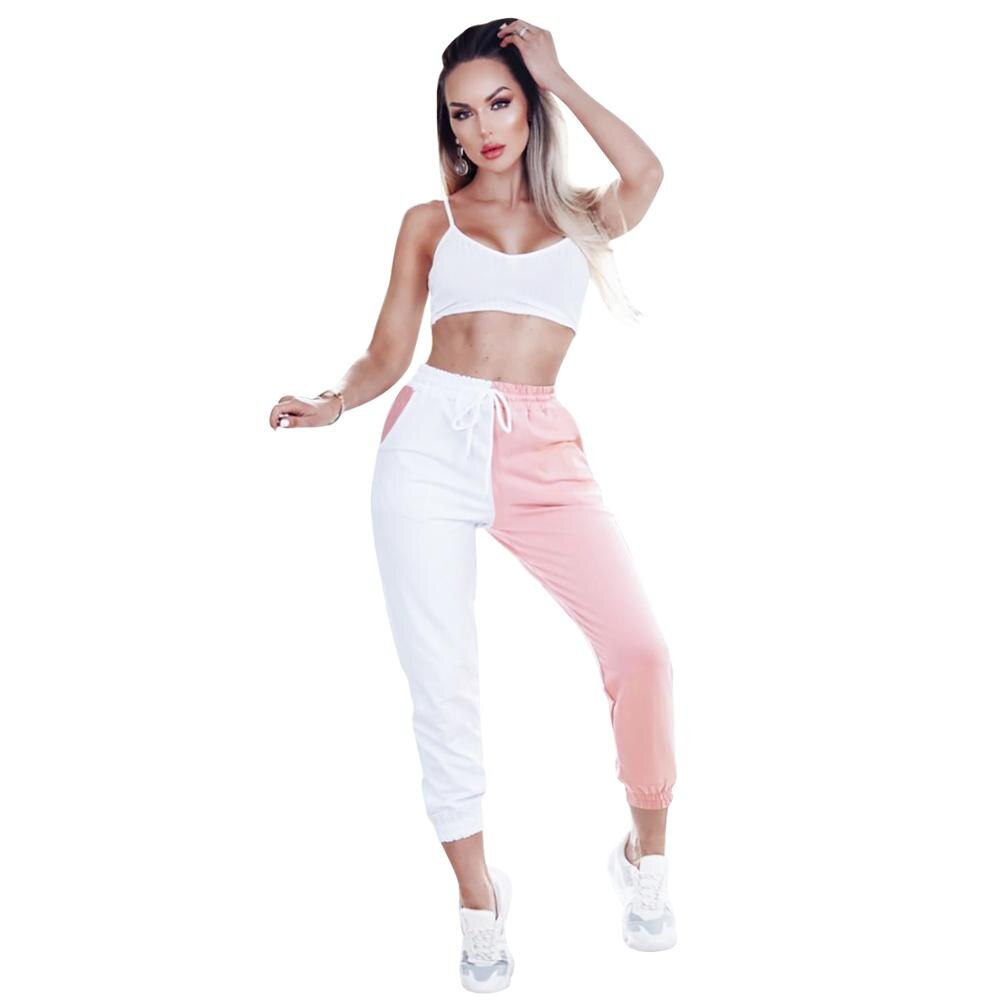 Woman wearing a white sports bra and pink and white jogger pants on a white background